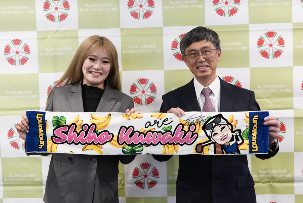 桑木志帆選手のサイン入りタオルを手に笑顔を浮かべる仁熊健文院長と桑木志帆選手